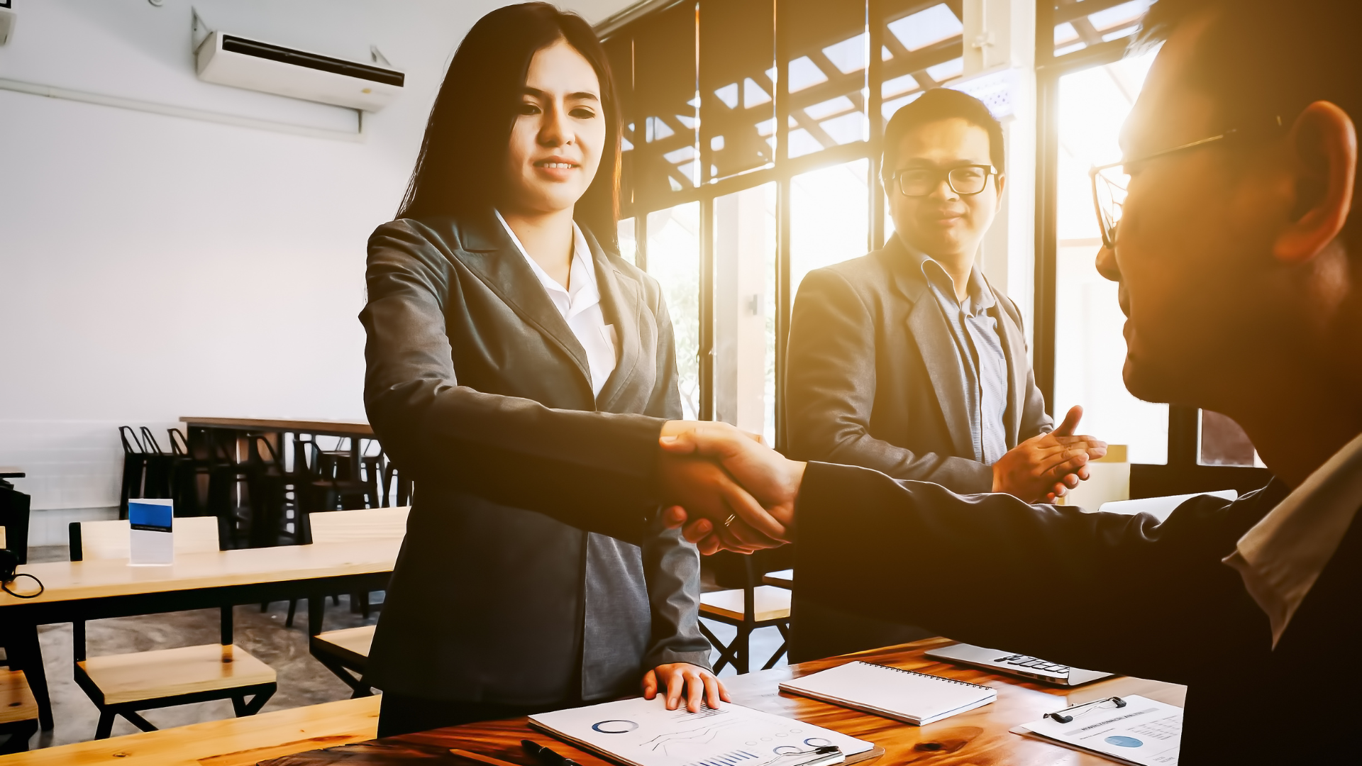 An Asian business woman shaking hands with an Asian business man.