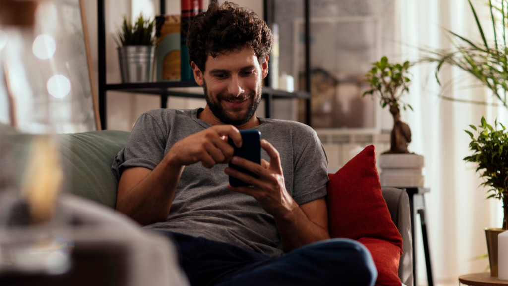 A man lazily sitting on the couch, scrolling on his phone.