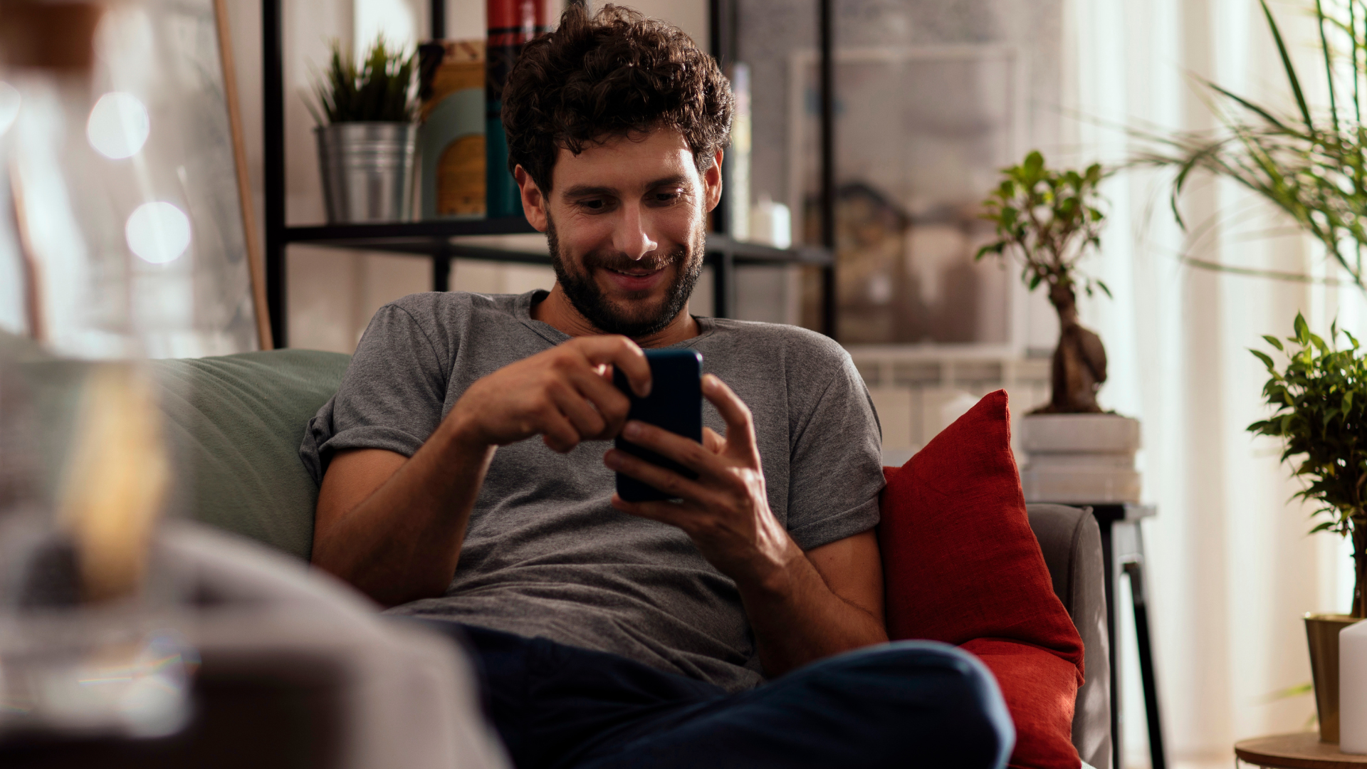 A man lazily sitting on the couch, scrolling on his phone.